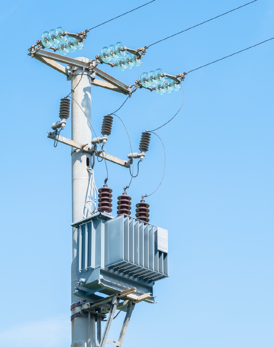 An electricity pole carrying a distribution transformer, insulators and overhead lines against a clear blue sky